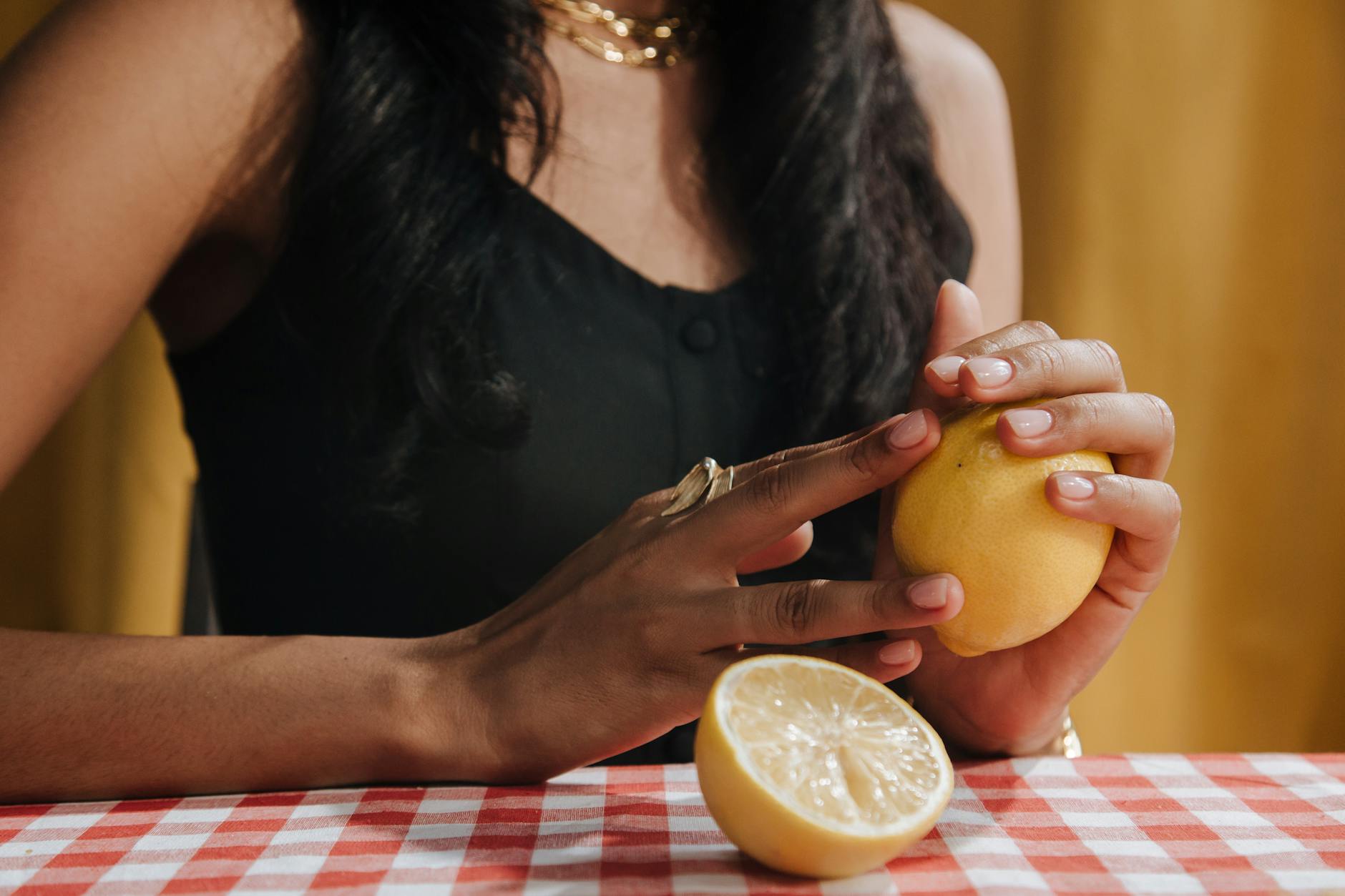 Una donna con i capelli neri che tiene un limone fresco a un tavolo da pranzo