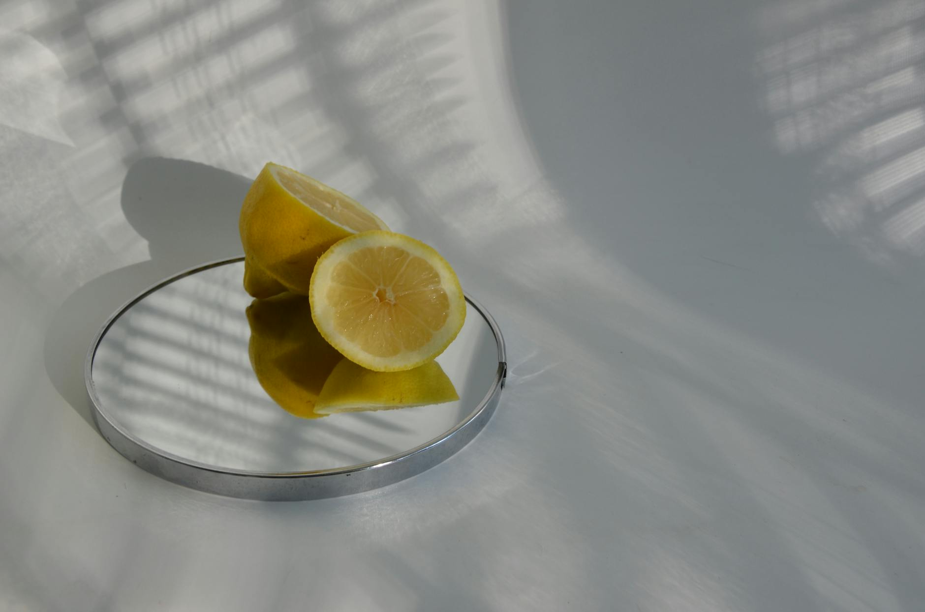 Una mano con unghie bianche che tiene un limone su uno sfondo rosa morbido, circondata da altri tre limoni