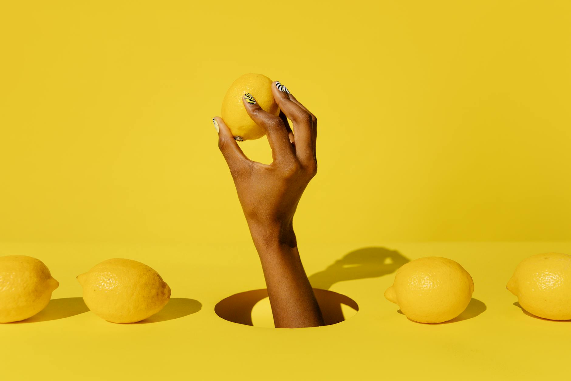 Una mano che tiene un limone fresco su uno sfondo giallo vivace, simbolo di rinascita e freschezza
