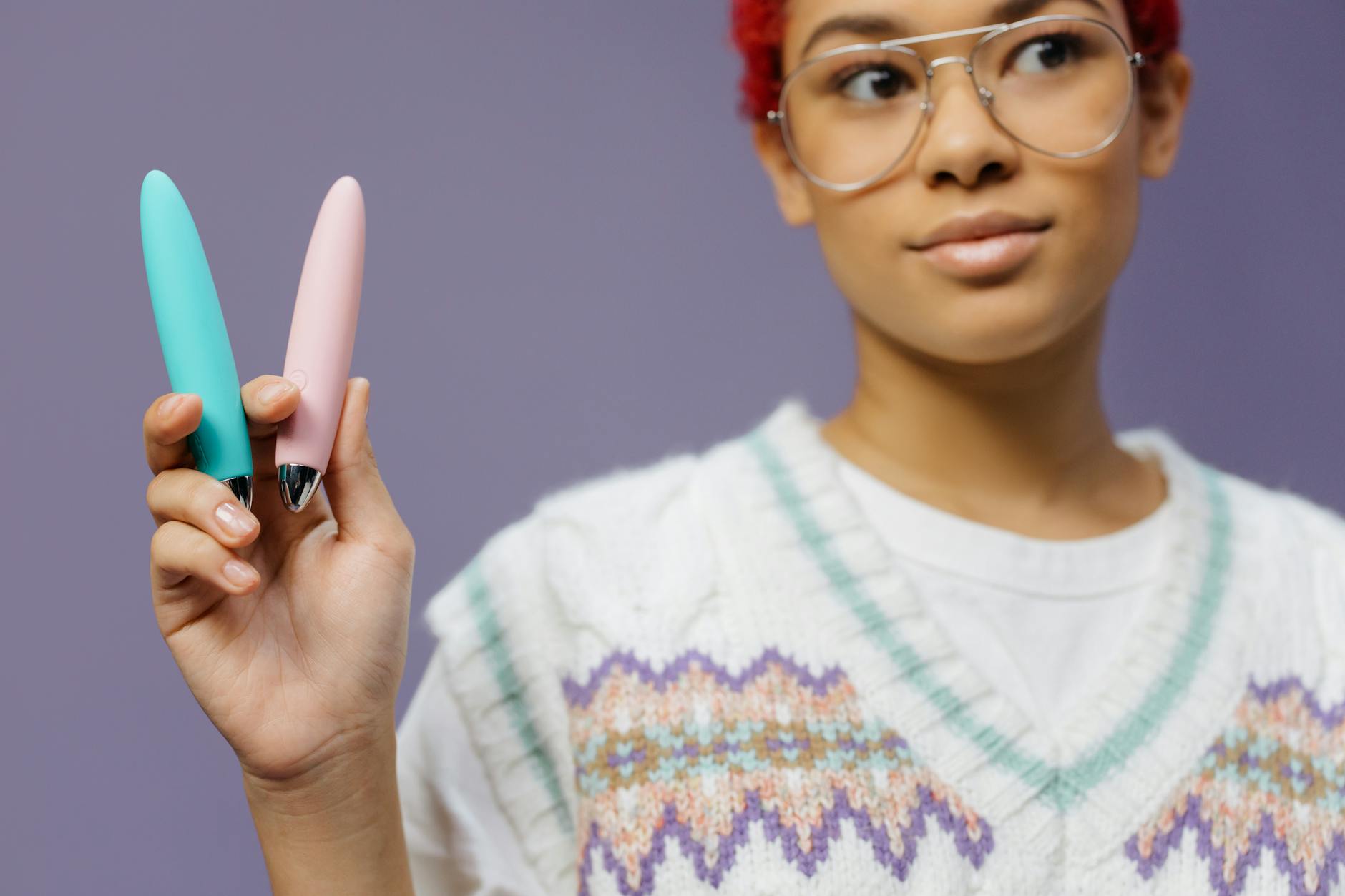Una donna con occhiali tiene due vibratori colorati su uno sfondo viola
